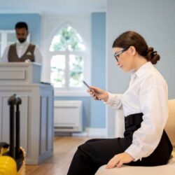 Businesswoman Using Smartphone Booking Room Sitting At Reception